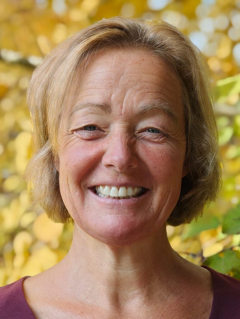 Lächelnde Frau vor herbstlich gelbem Blätterhintergrund, freundlich in die Kamera blickend.